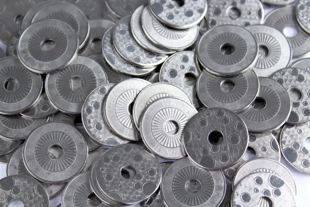 A pile of stainless steel latent image tokens. All tokens are the same model. The tokens have one side with bubbles. Of the tokens that show the other side, some show the text "car wash" some don't, depending on how they lie in the pile and how the light hits them.